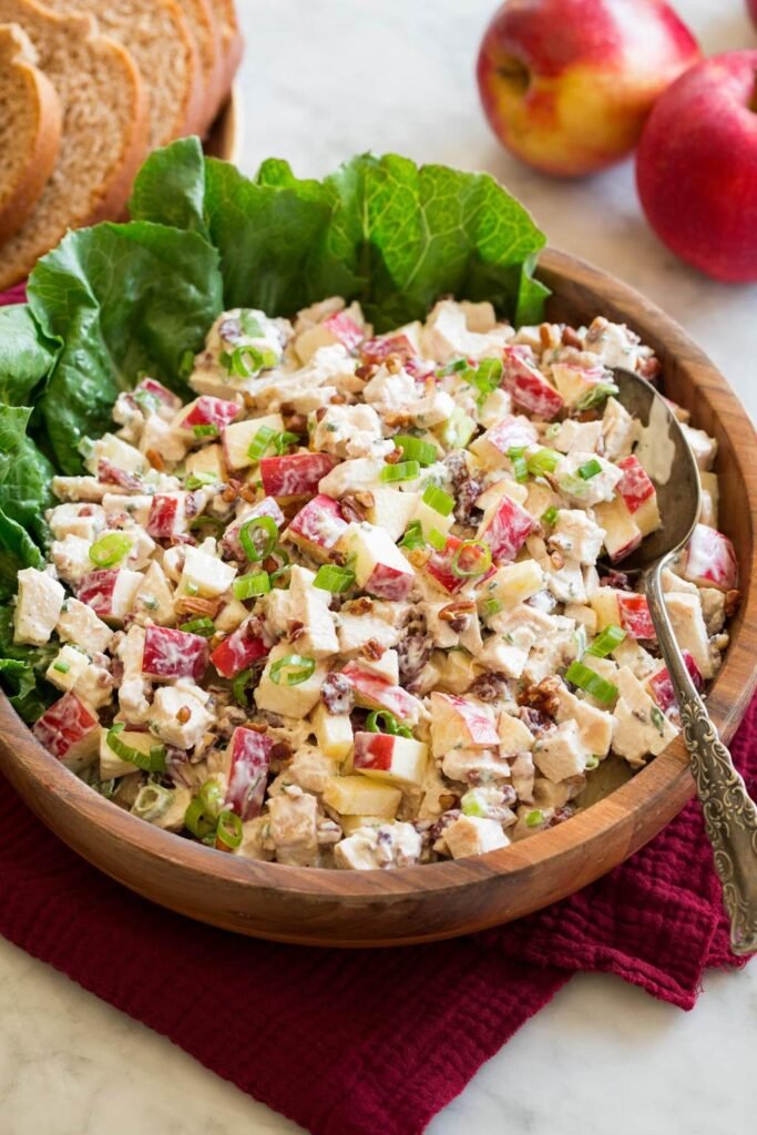 Creamy chicken salad with diced apples, celery, walnuts, and green onions in a wooden bowl lined with lettuce leaves.