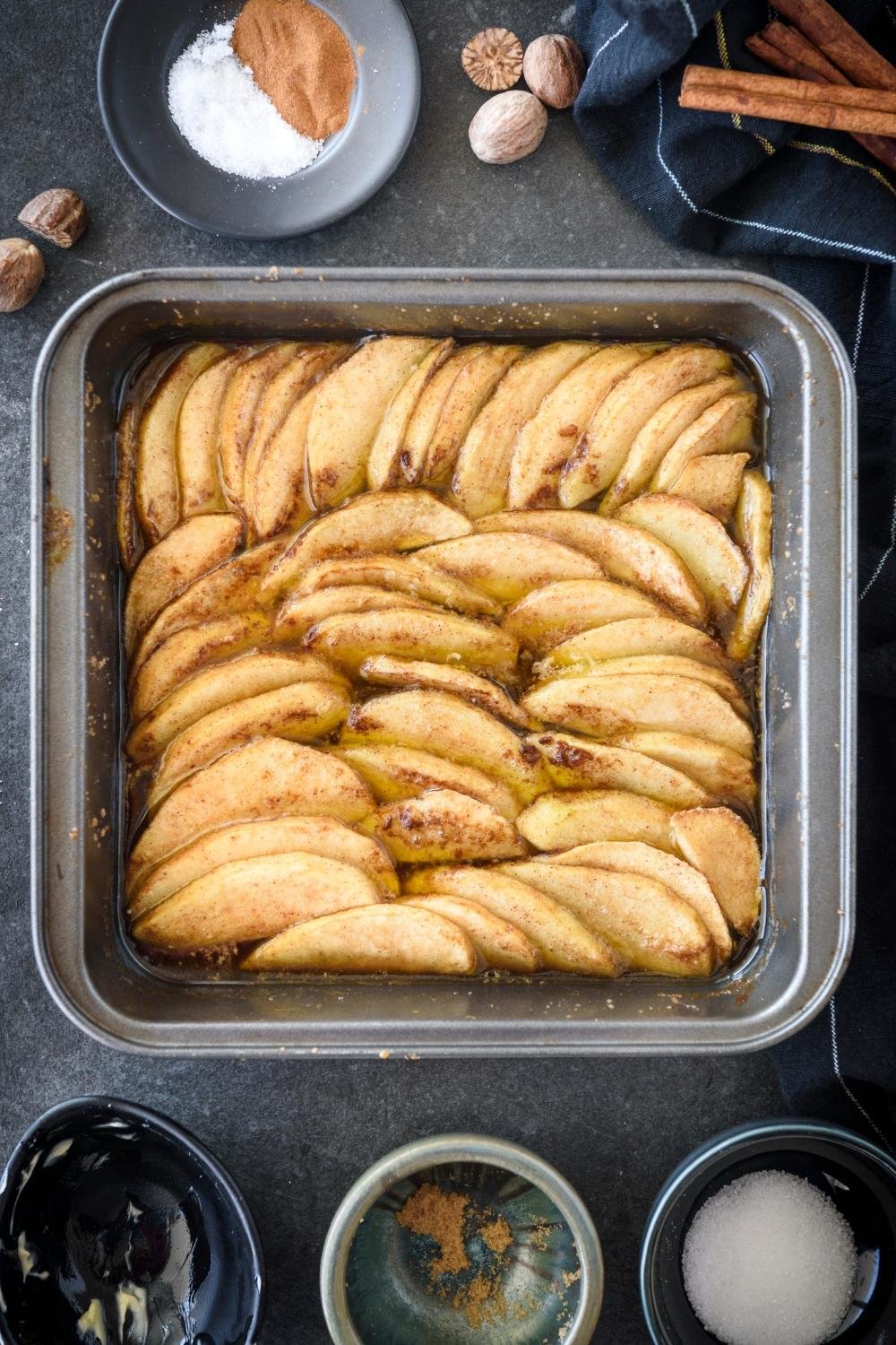Pan of neatly arranged apple slices baking in a shallow dish with cinnamon.