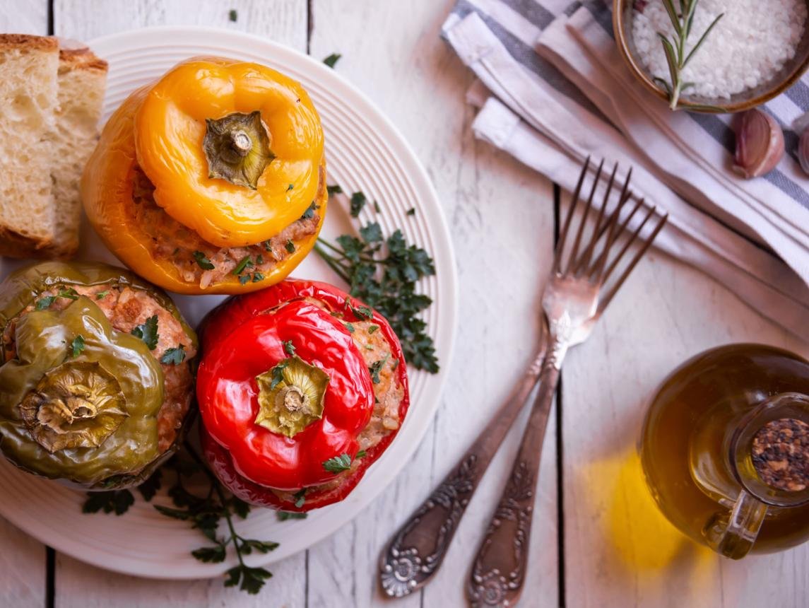 Plate with colorful stuffed bell peppers (yellow, red, green) and slices of bread on a rustic table, garnished with herbs and a salt bowl nearby.