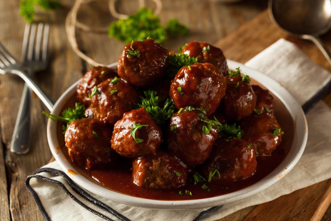 Meatballs in rich tomato sauce garnished with chopped parsley on a white plate. rustic wooden table in the background.