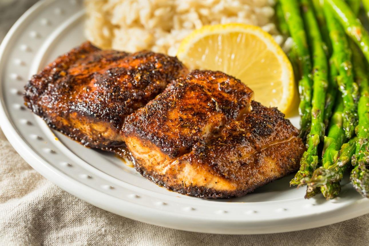 Grilled chicken breasts with a lemon slice, asparagus, and rice on a white plate.