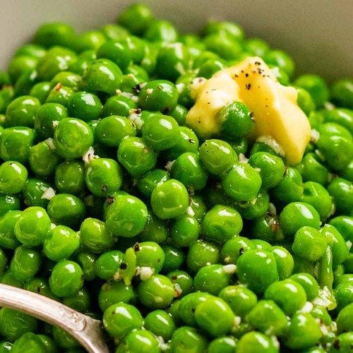 A bowl of bright green peas tossed with a pat of melted butter and a few black Pepper specks.