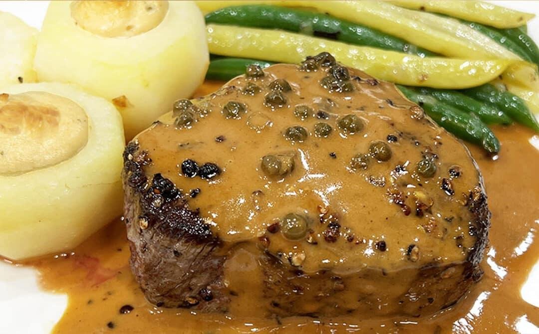 Pan-seared beef filet with creamy peppercorn sauce, served with potatoes and green beans on a plate