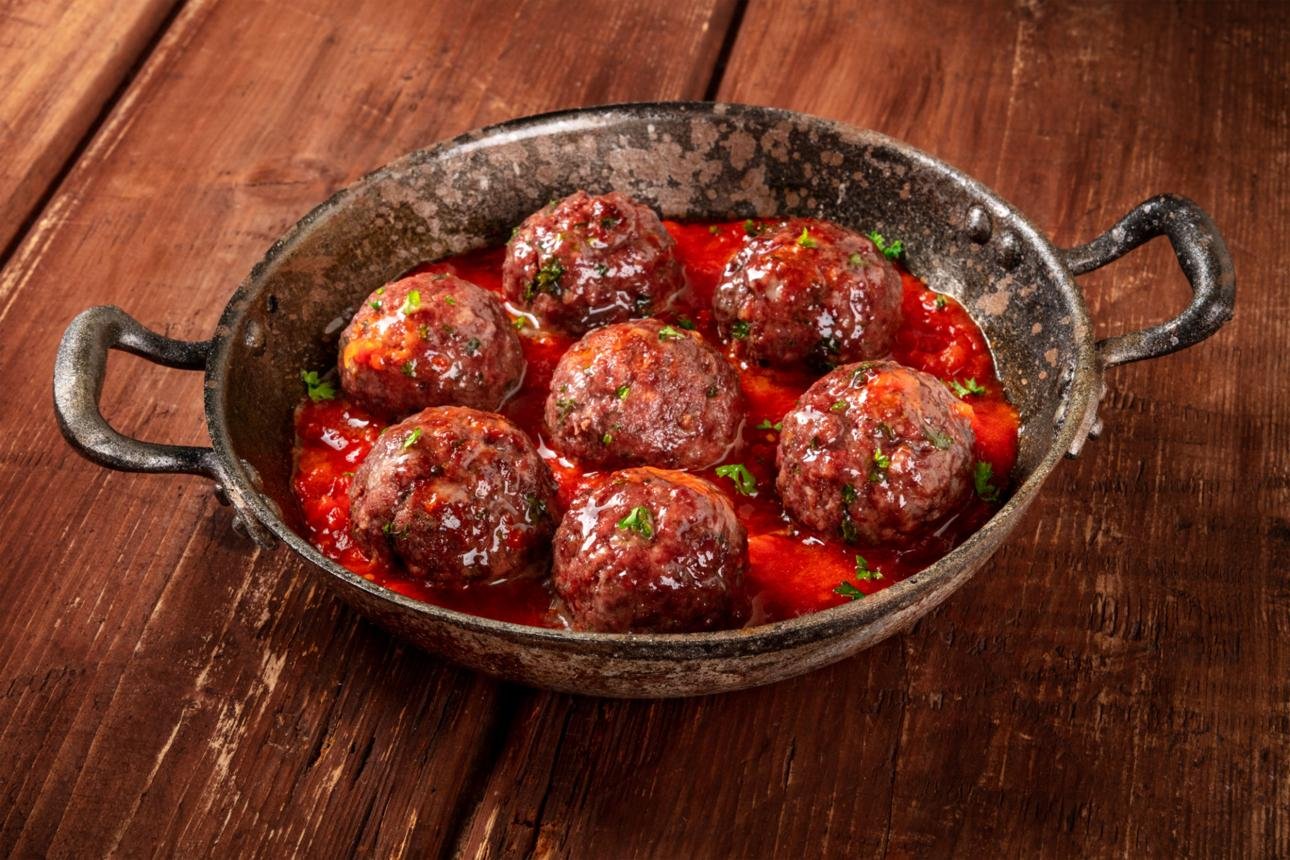 Meatballs simmering in red tomato sauce in a rustic pan, garnished with parsley on a wooden table