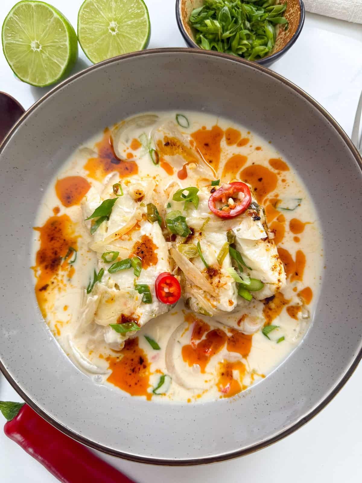 Creamy white fish in a lime-chili sauce, garnished with chili rings and green onions, in a gray bowl with lime halves nearby.