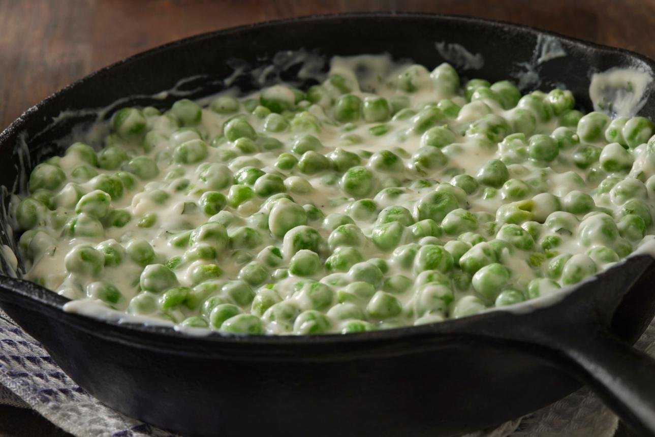 Peas in a creamy white sauce cooking in a black cast-iron skillet on a wooden surface