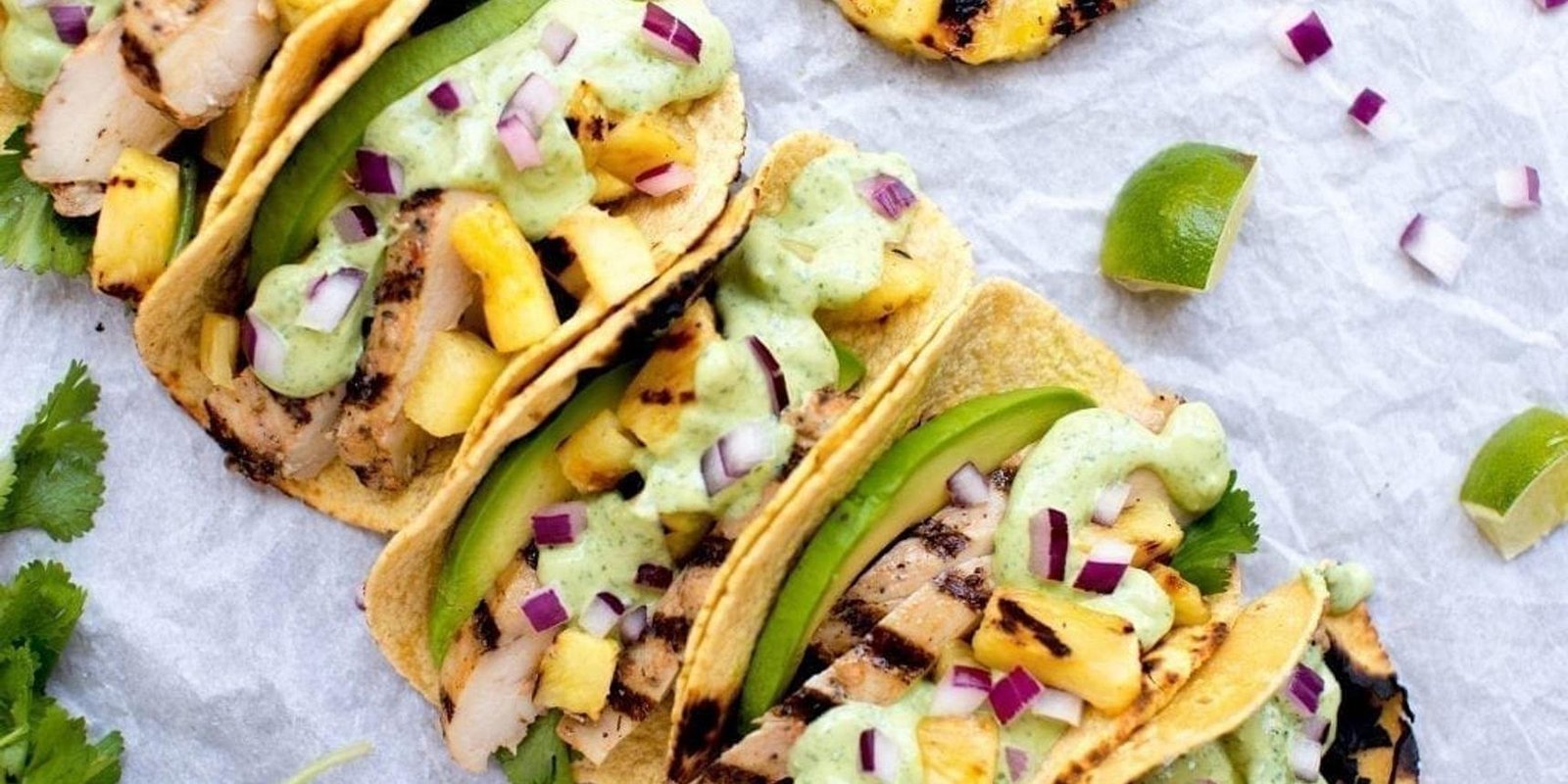 Grilled chicken tacos with pineapple, avocado, red onion, cilantro, and a green crema on warm corn tortillas.