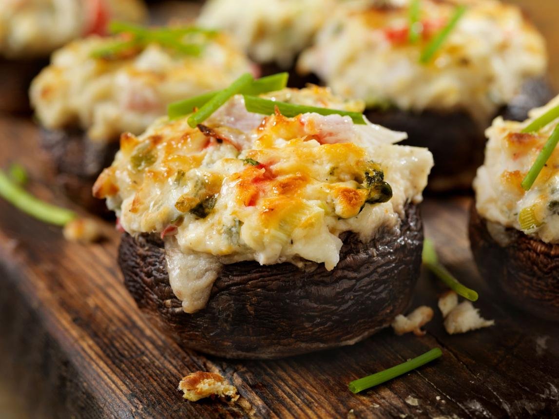 Stuffed mushroom caps filled with creamy cheese and herbs on a wooden board.