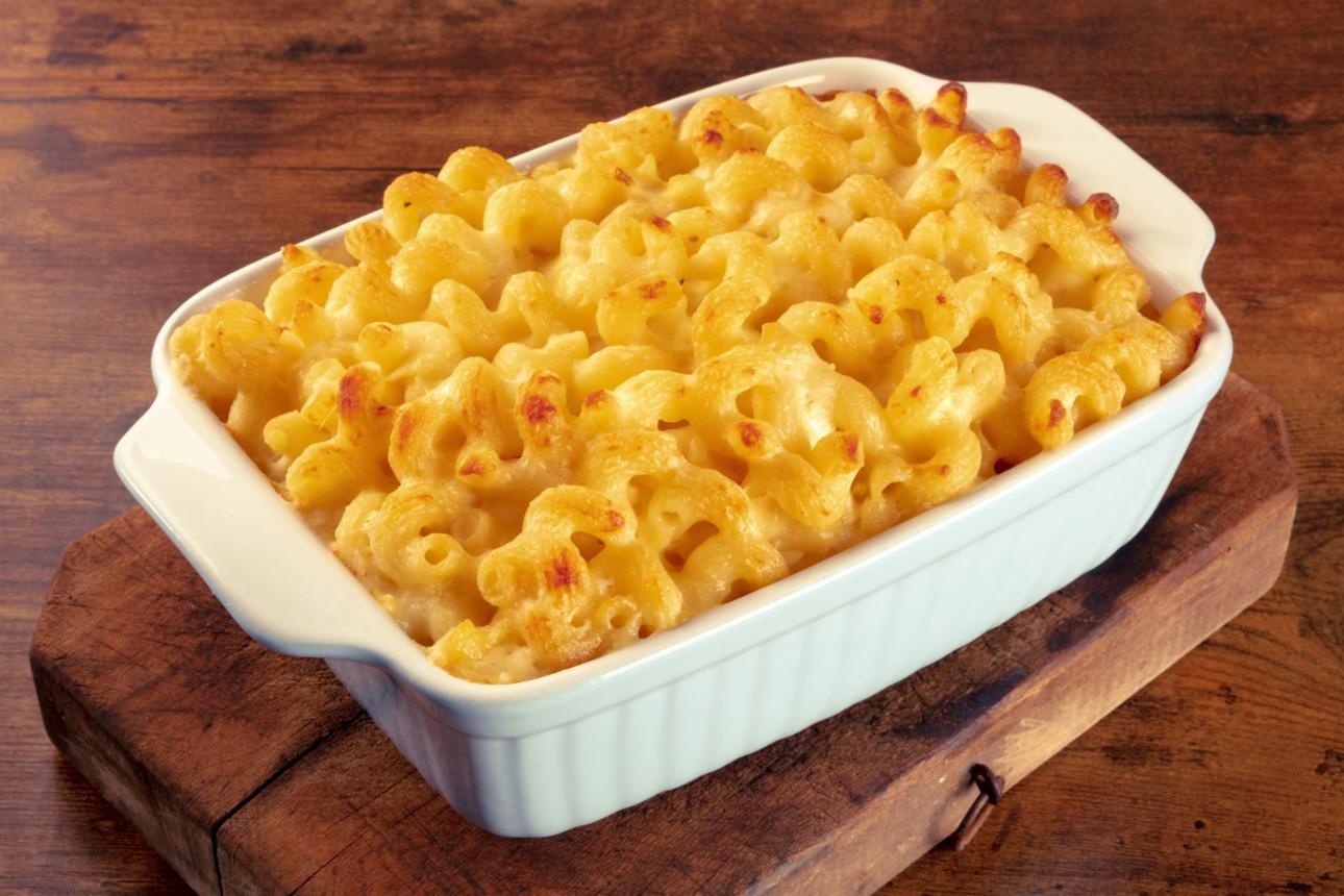 Creamy baked macaroni and cheese in a white oval casserole on a wooden board, golden-browned top.