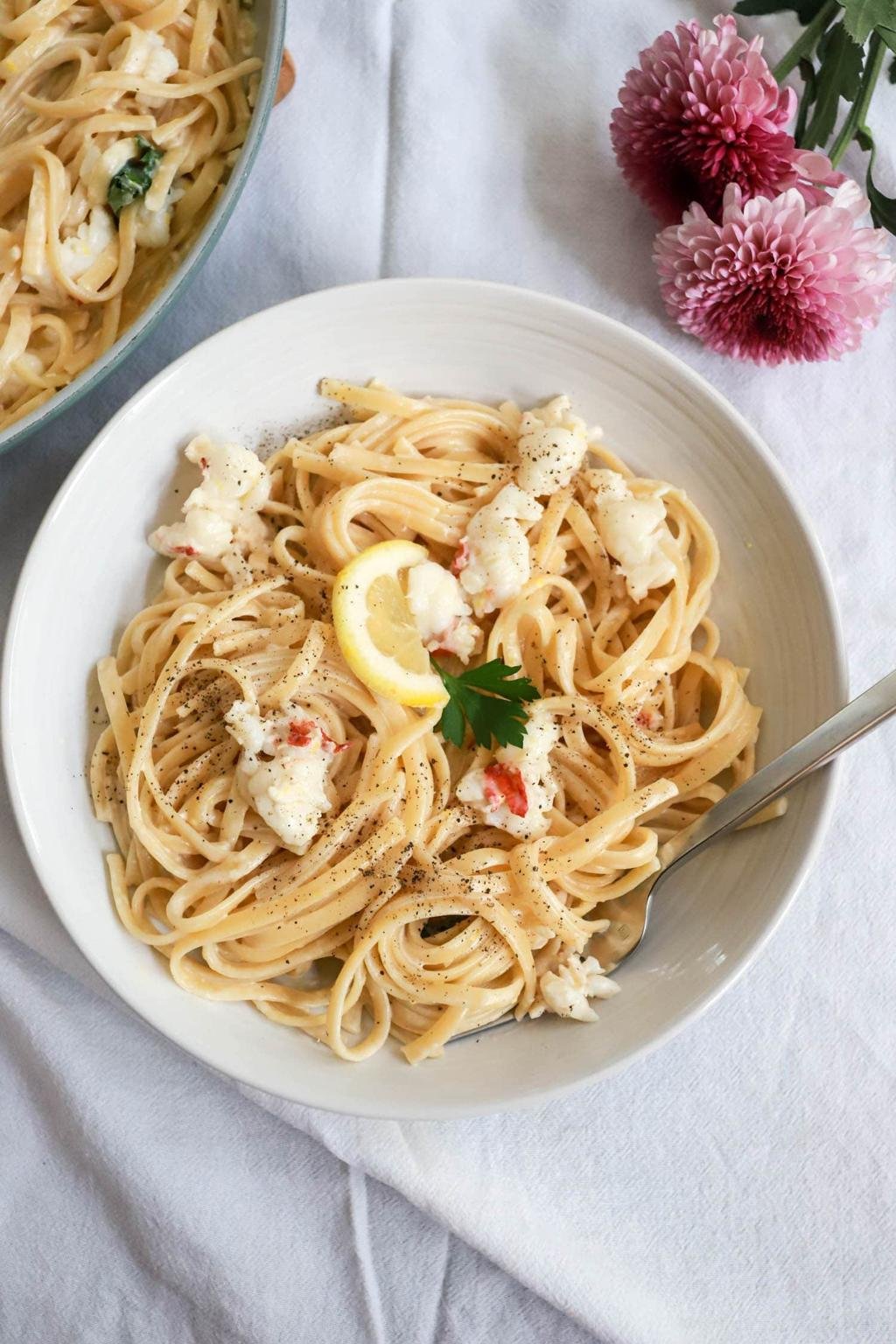 Linguine with crab meat in a light sauce, garnished with lemon, parsley, and cracked pepper on a white plate.