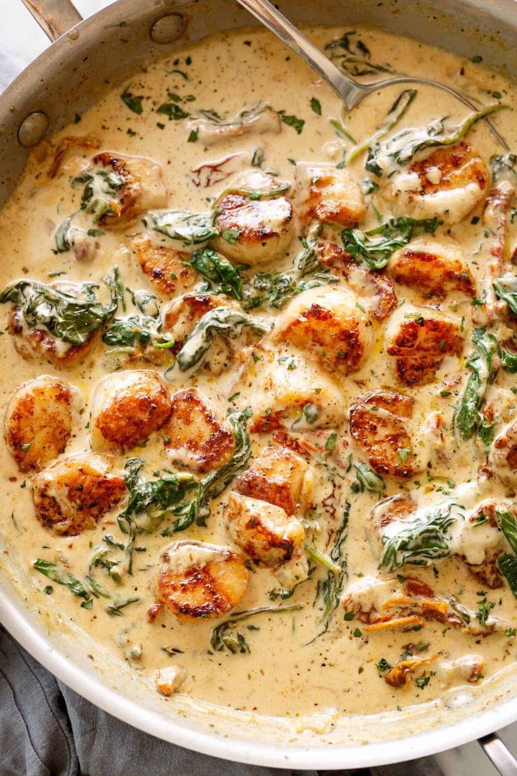 Skillet of seared scallops in a creamy herb sauce with spinach and parsley flakes