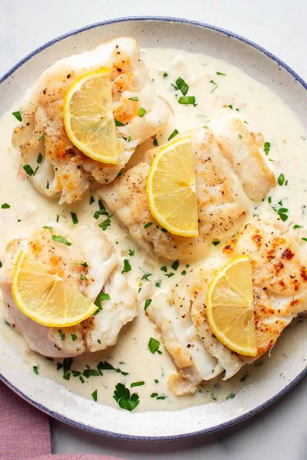 Pan-seared white fish fillets in a creamy lemon-butter sauce, topped with lemon wedges and chopped parsley.