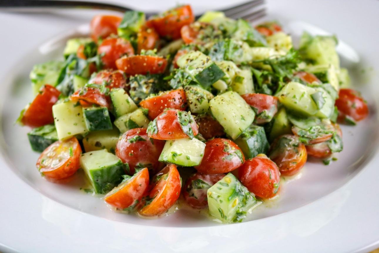 Cucumber, avocado, and cherry tomato salad tossed in herbs on a white plate.