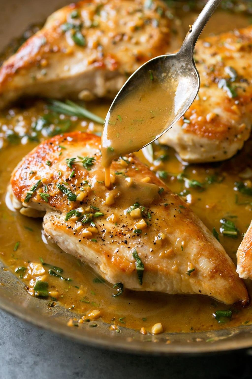 Pan-seared chicken breasts in a creamy herb sauce, with chopped nuts and parsley, as sauce is spooned over them.