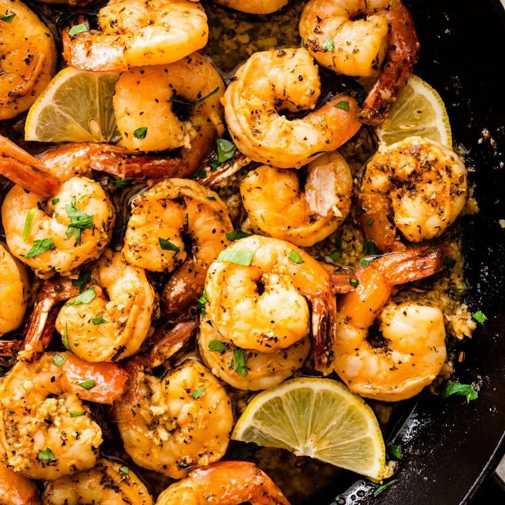 Shrimp sautéed with garlic and herbs in a skillet, topped with lemon wedges and parsley