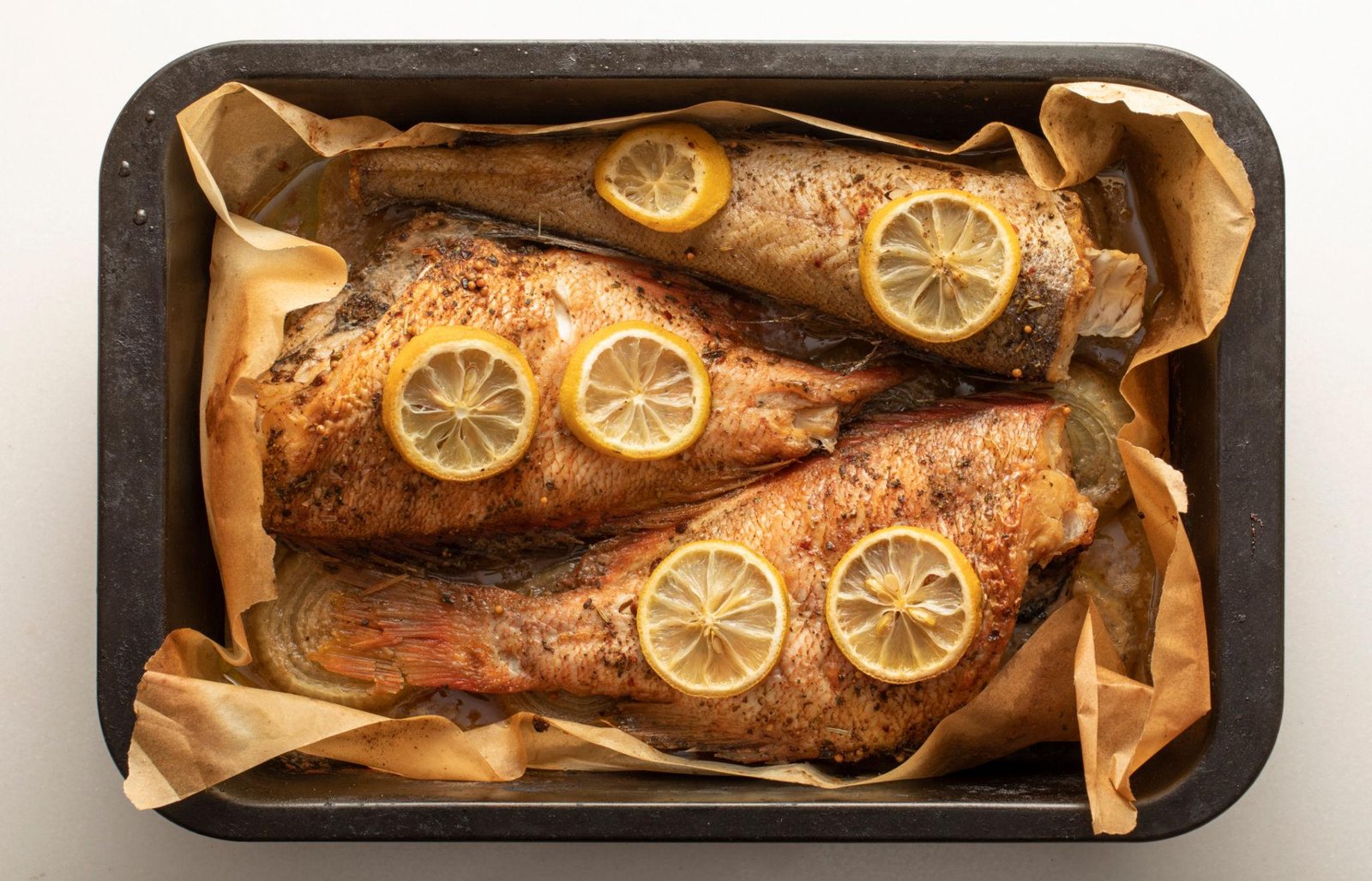 Two whole roasted fish with lemon slices, baked in a parchment-lined pan.
