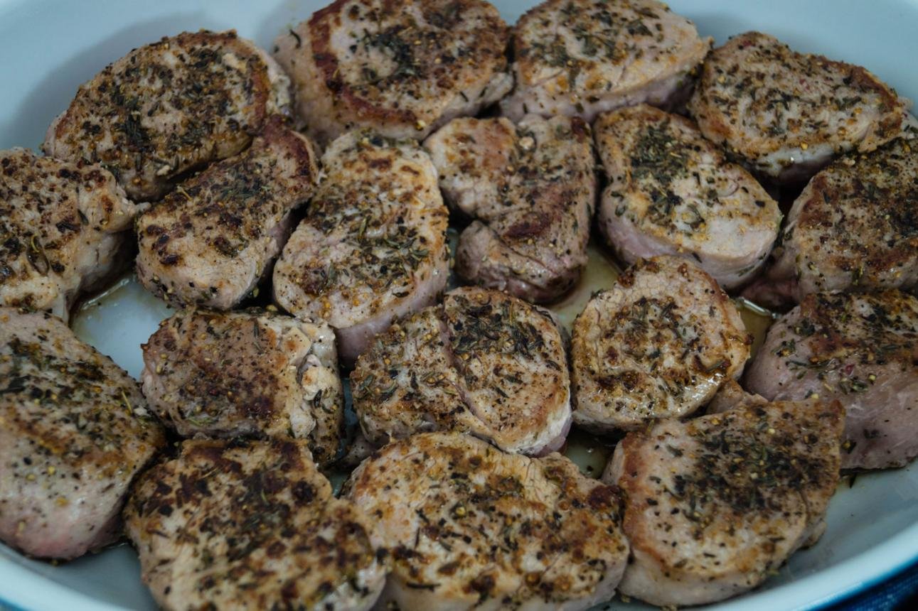 Sliced pork tenderloin medallions seasoned with herbs in a shallow baking dish