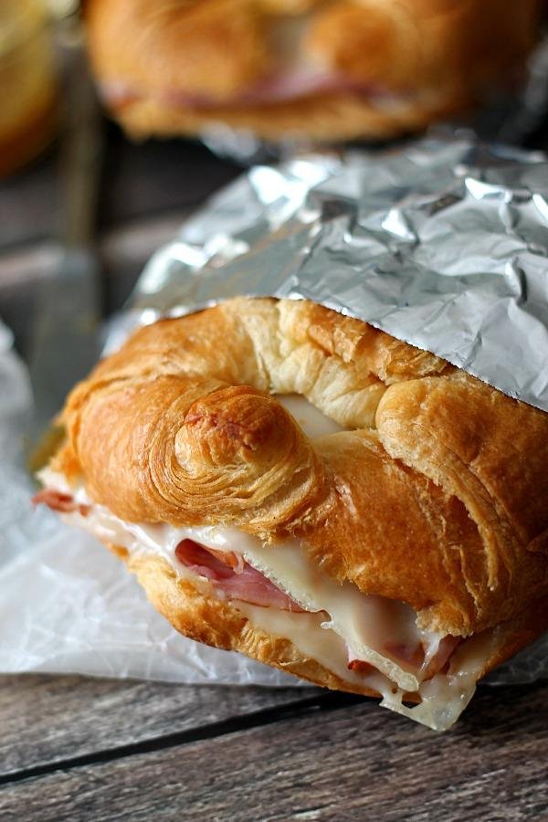 Croissant sandwich with melted cheese and ham, partially unwrapped from foil on a wooden surface.
