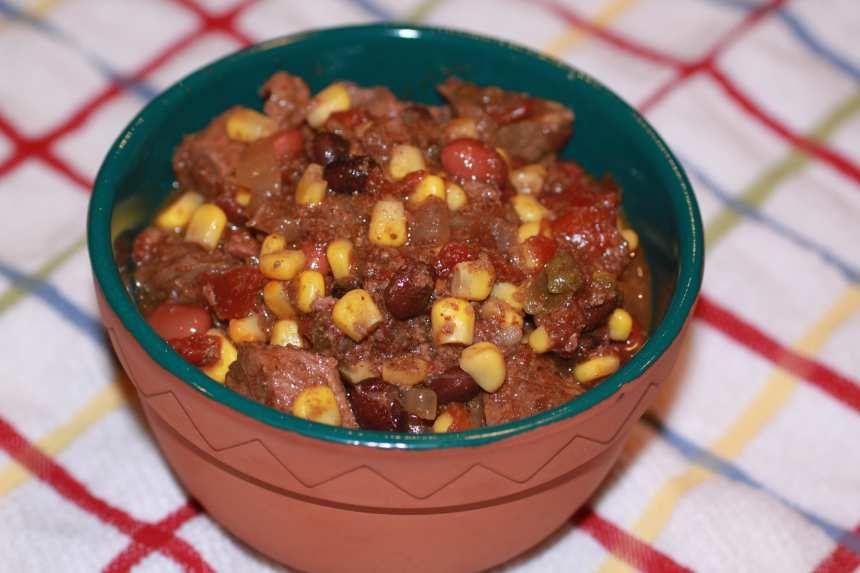 Bowl of chili with corn, beans, and beef on a checkered tablecloth surface