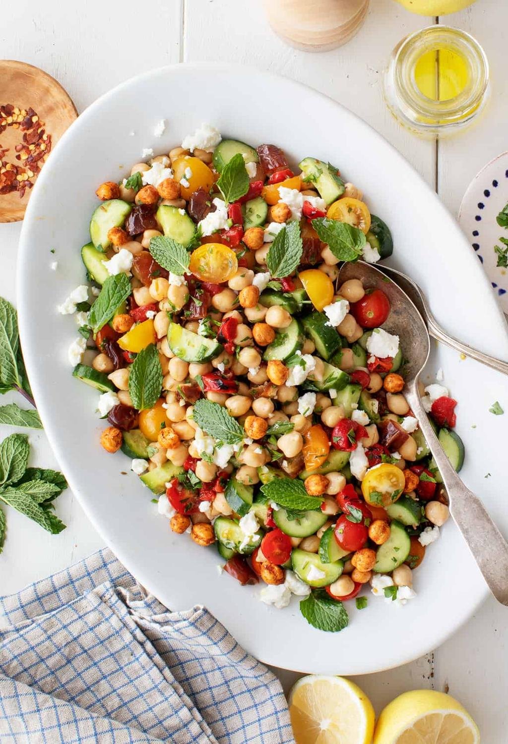 Colorful chickpea salad with cucumber, cherry tomatoes, feta, and fresh mint on a white platter.