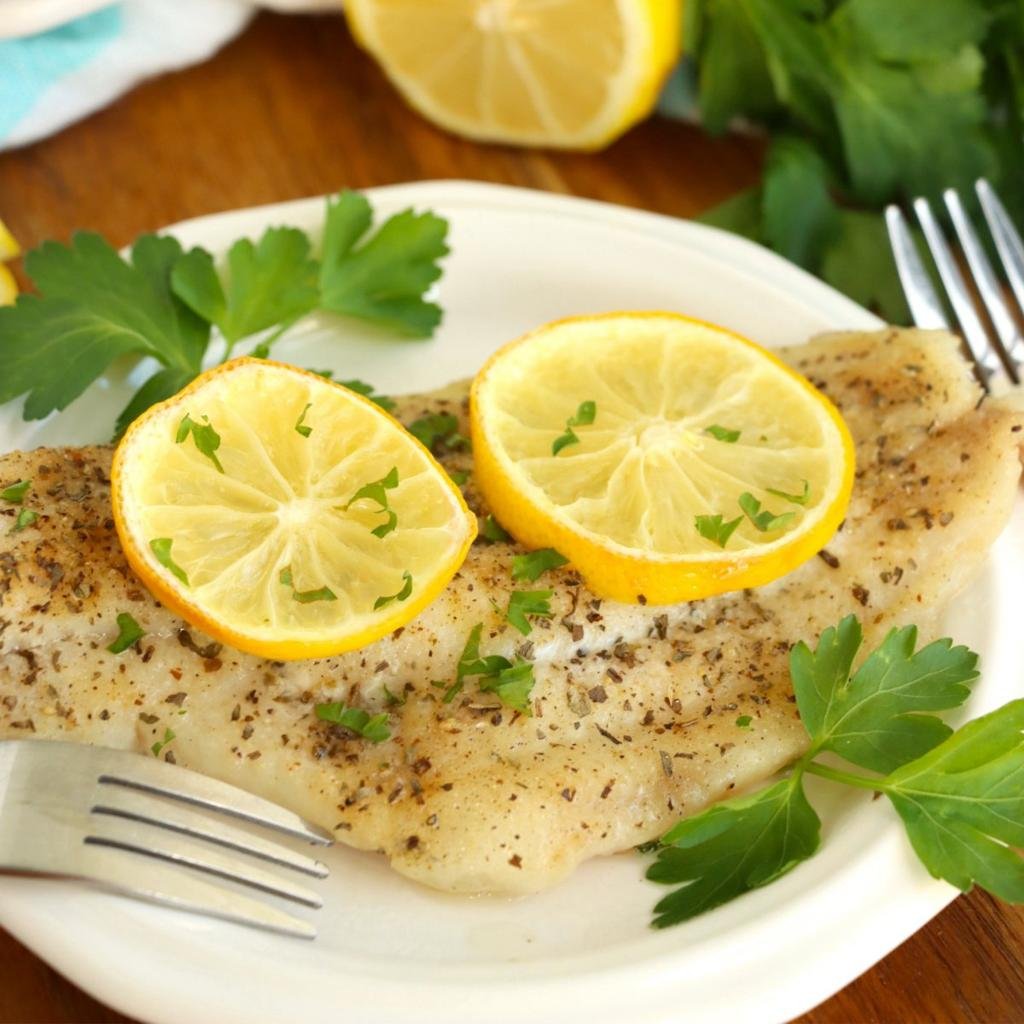 Pan-seared white fish fillet garnished with lemon slices and parsley on a white plate.