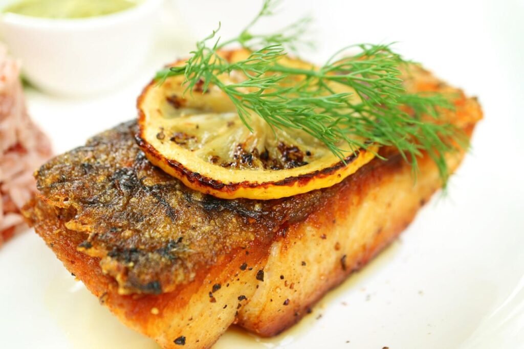 Crispy fried fish fillet topped with a lemon slice and a sprig of dill on a white plate