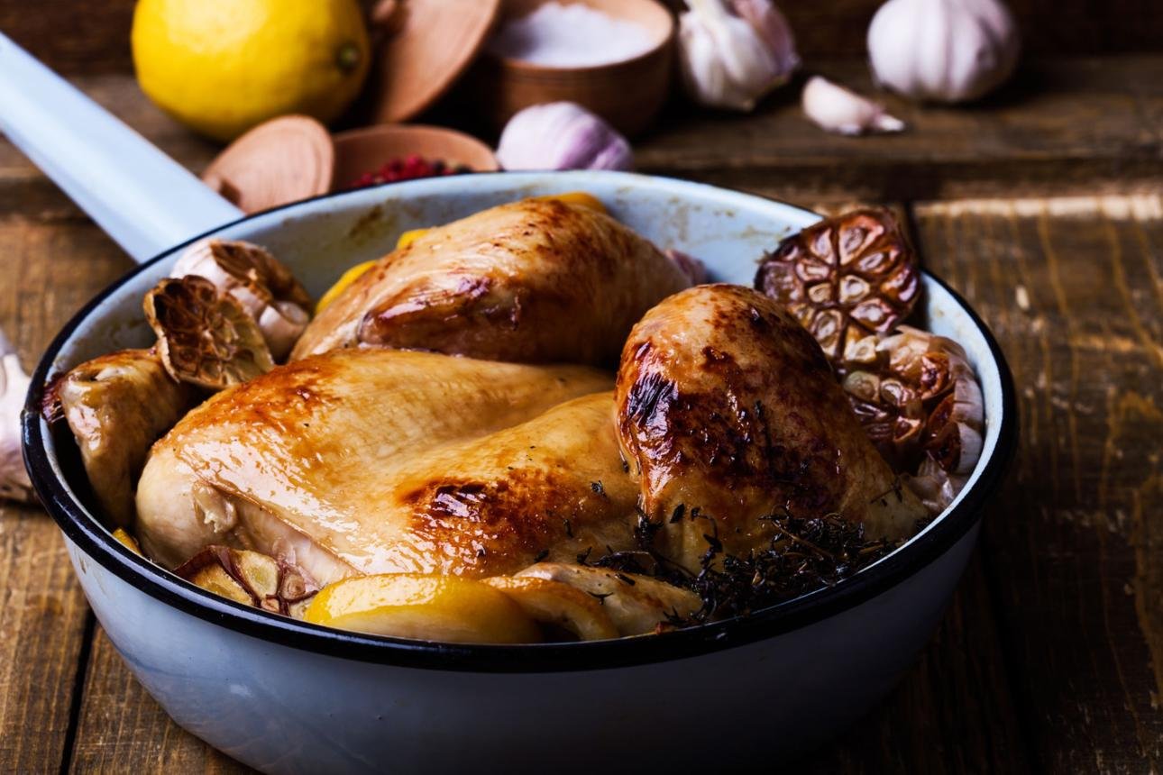 Roasted whole chicken in a blue enamel pan with lemon wedges, garlic, and thyme on a rustic wooden table (food photography)
