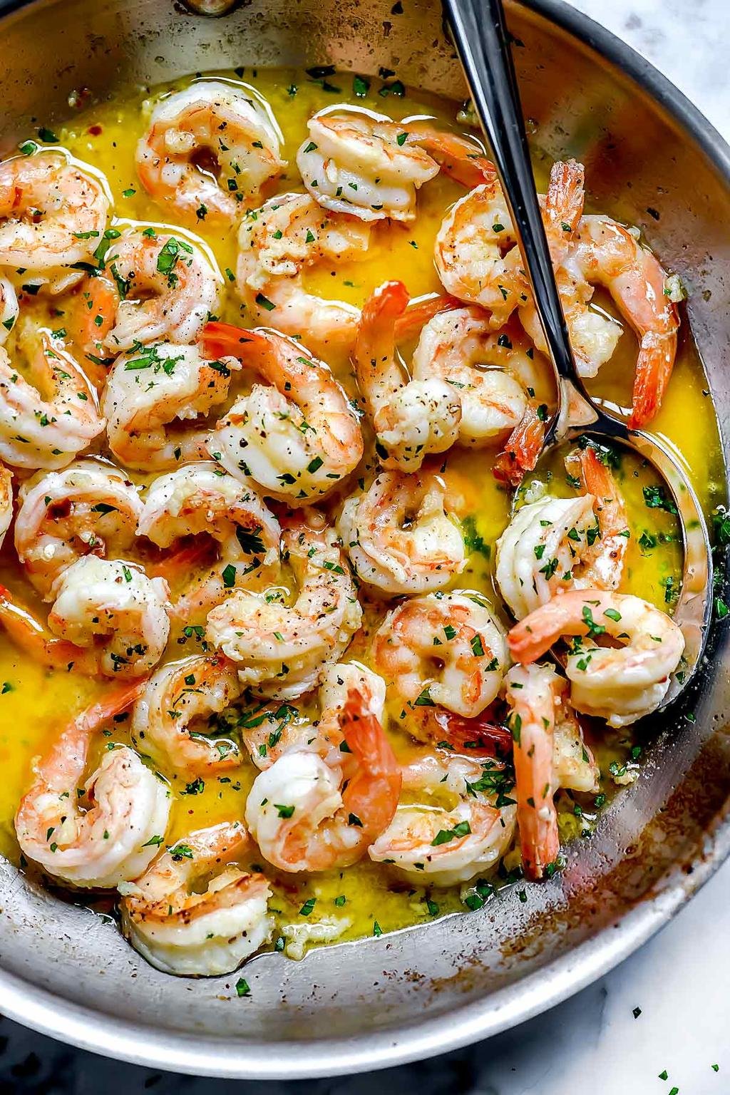 Shrimp in lemon-butter sauce cooking in a skillet, sprinkled with chopped parsley.
