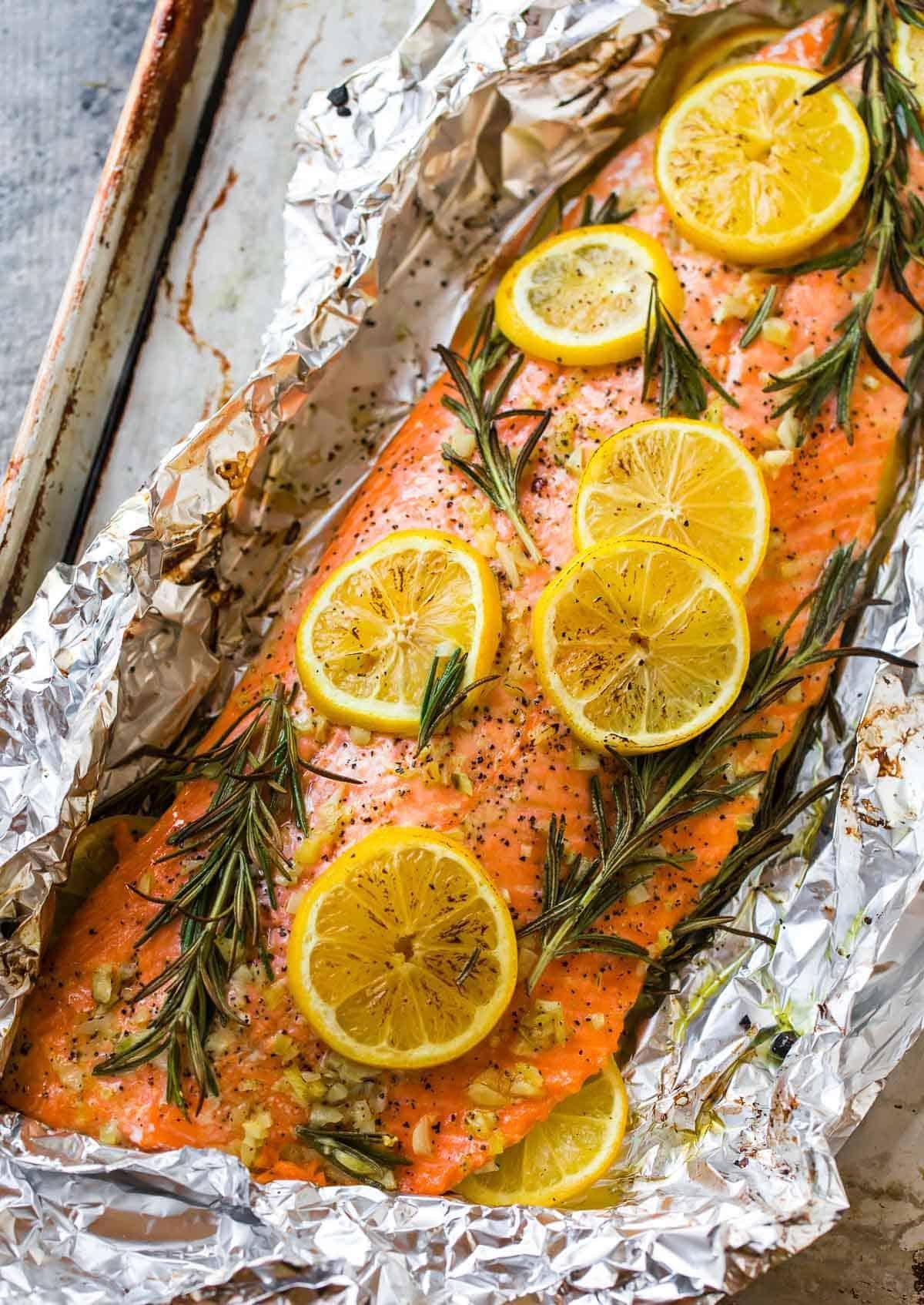 Baked salmon fillet on foil with lemon rounds and rosemary sprigs, ready for roasting.