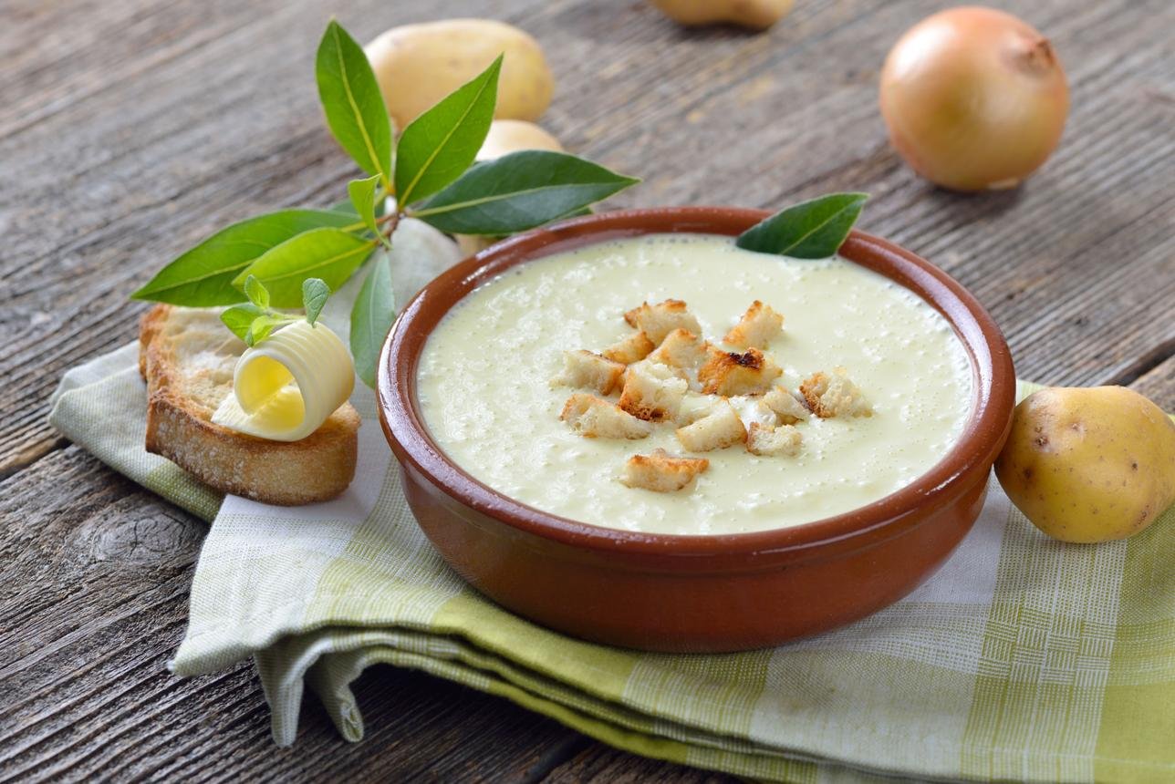 Creamy potato soup with croutons in a brown ceramic bowl on a rustic wooden table, with bread and butter nearby.