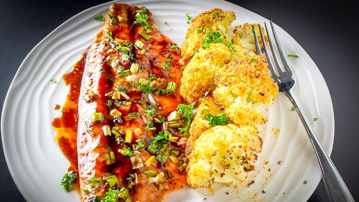 Salmon fillet with a red glaze and chopped green onions, served with roasted cauliflower on a white plate.