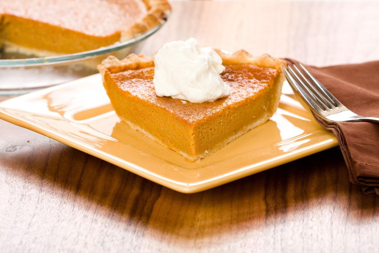 Slice of pumpkin pie topped with whipped cream on a yellow plate with a fork nearby.
