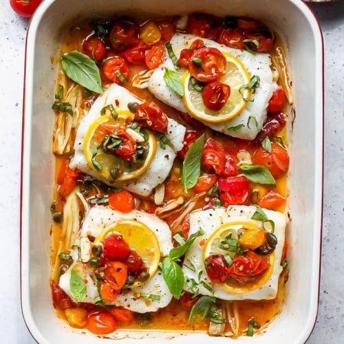 Baked white fish fillets with lemon rounds, cherry tomatoes, and fresh basil in a tomato-herb sauce