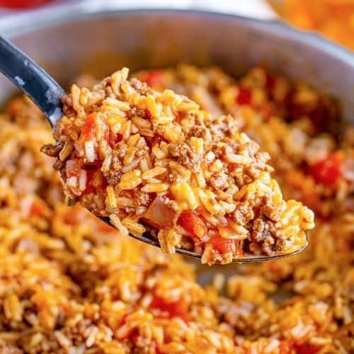 Close-up of a spoonful of fried rice with ground beef, corn, and red peppers lifted from a pot.