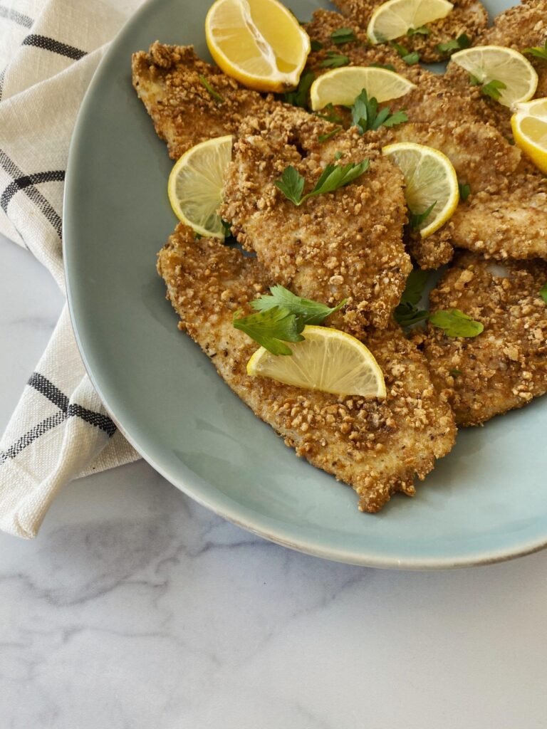 Crispy breaded chicken cutlets on a blue plate, garnished with lemon wedges and parsley slices
