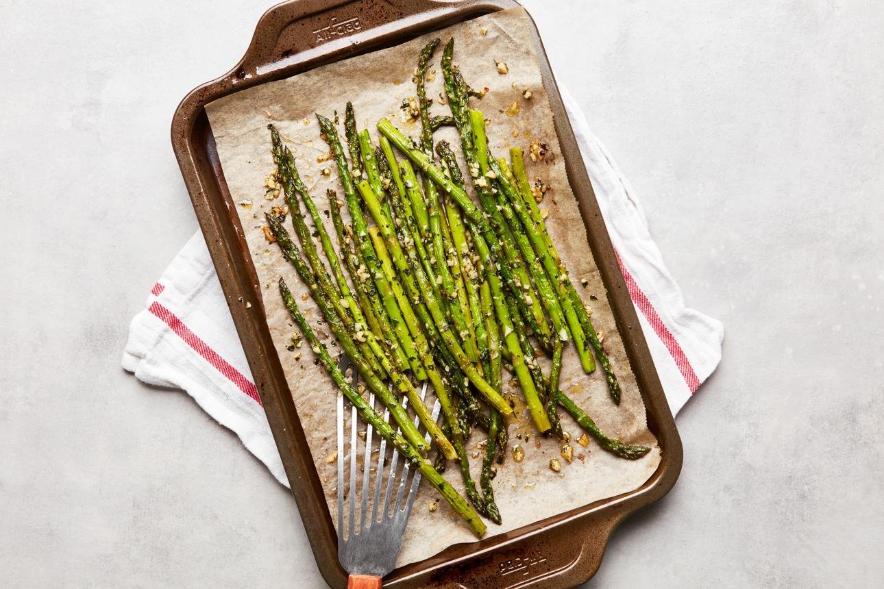 Roasted asparagus spears on a parchment-lined baking sheet with garlic crumbs nearby