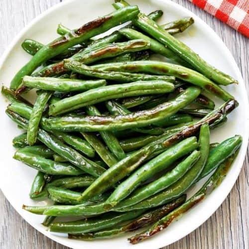 Plate of sautéed green beans with a few brown spots on a white plate, napkin visible in the corner.