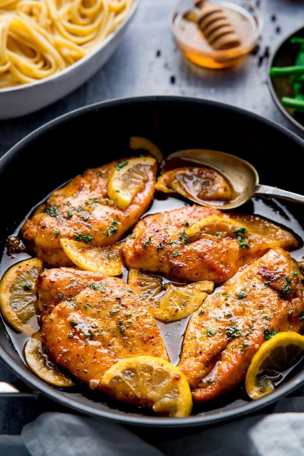 Pan-seared chicken breasts in a dark skillet with lemon slices, herbs, and a light lemony glaze.