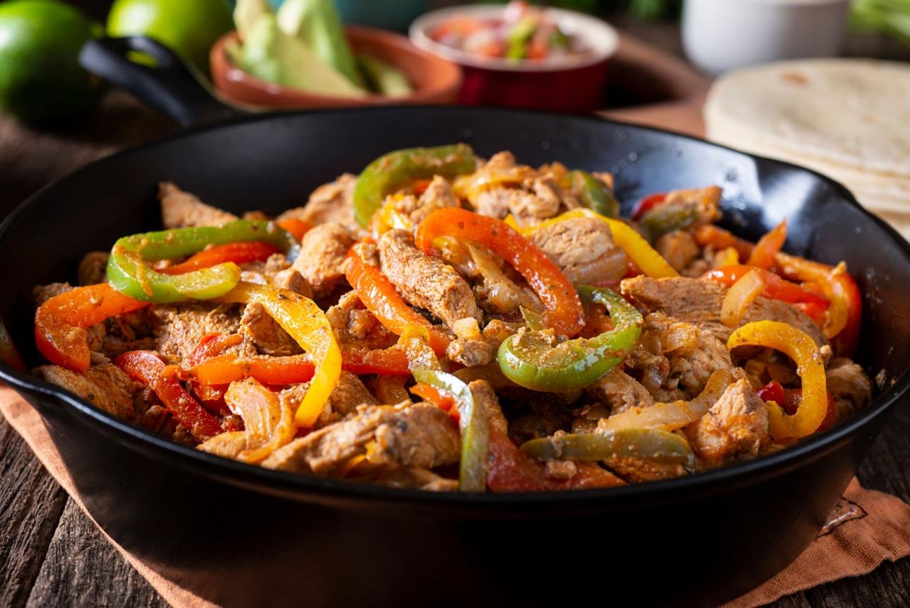 Skillet of pork strips with colorful bell peppers (red, yellow, green) sautéed in a sauce.