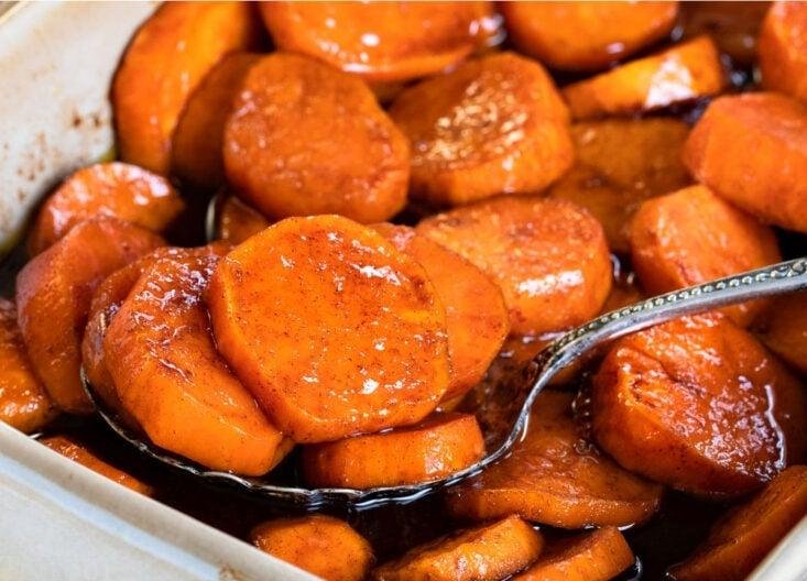 Glazed orange carrot coins in a baking dish with a metal serving spoon