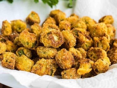 Pile of golden, breadcrumb-coated fried bite-sized snacks on a white plate, some with green centers showing through the coating.