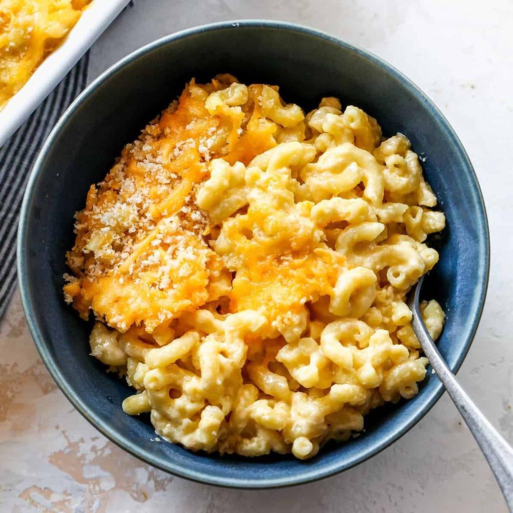 Blue bowl of creamy macaroni and cheese topped with toasted breadcrumbs, with a spoon resting on the side.