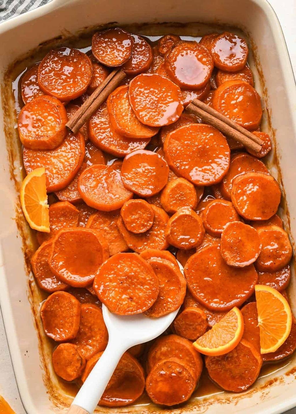 Baking dish of orange-glazed carrot rounds with cinnamon sticks and orange wedges for garnish, ready to bakewise mix of spice and sweetness.