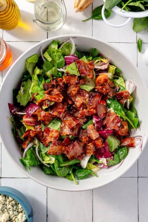 Salad bowl with mixed greens, red onions, cherry tomatoes, and crispy bacon on top.