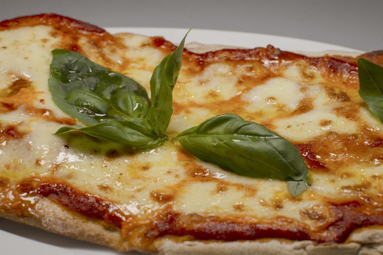 Close-up of a cheese pizza topped with fresh basil leaves and a golden crust.