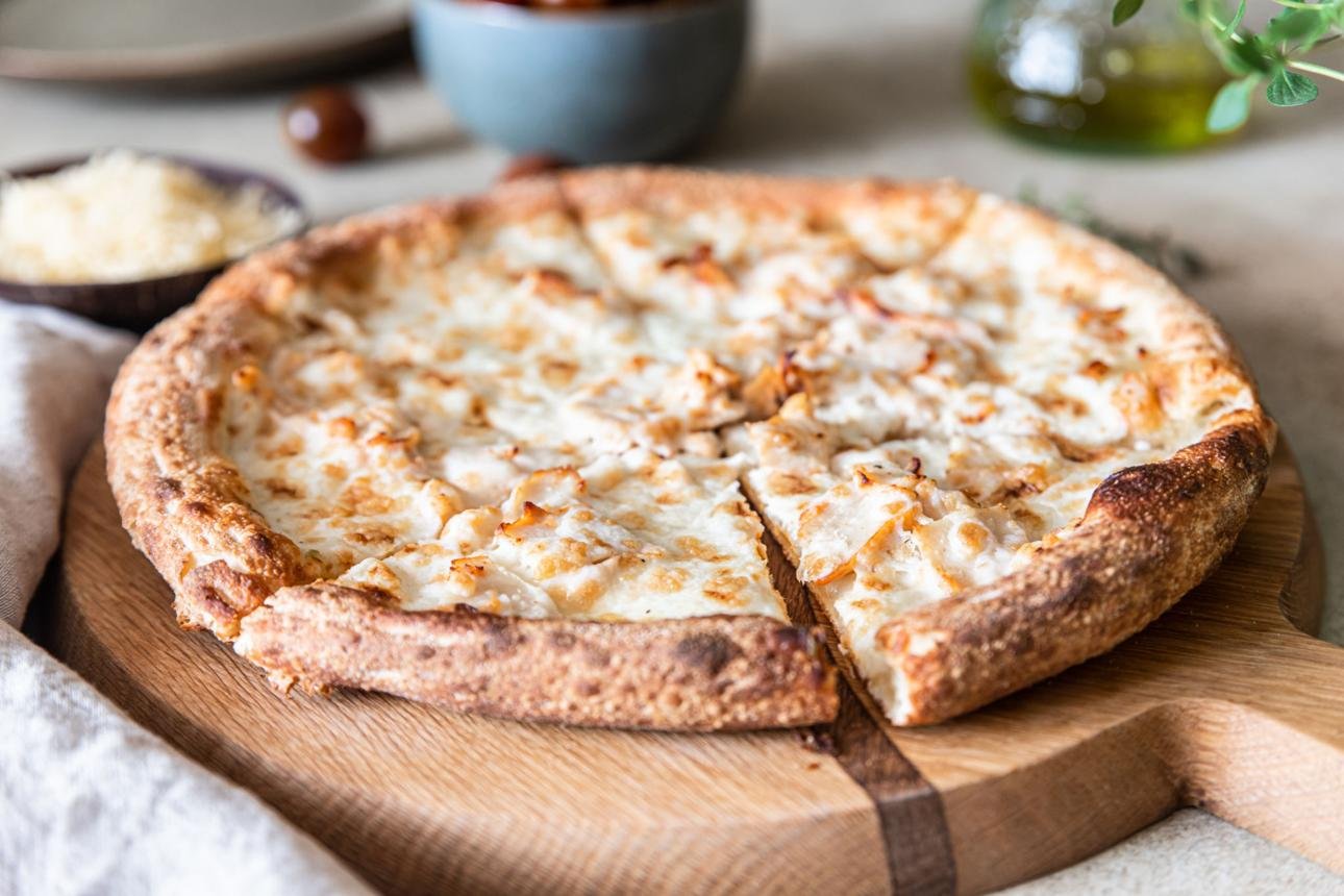 Cheese pizza on a round wooden board with a slice removed, showing bubbly browned crust and melted cheese.